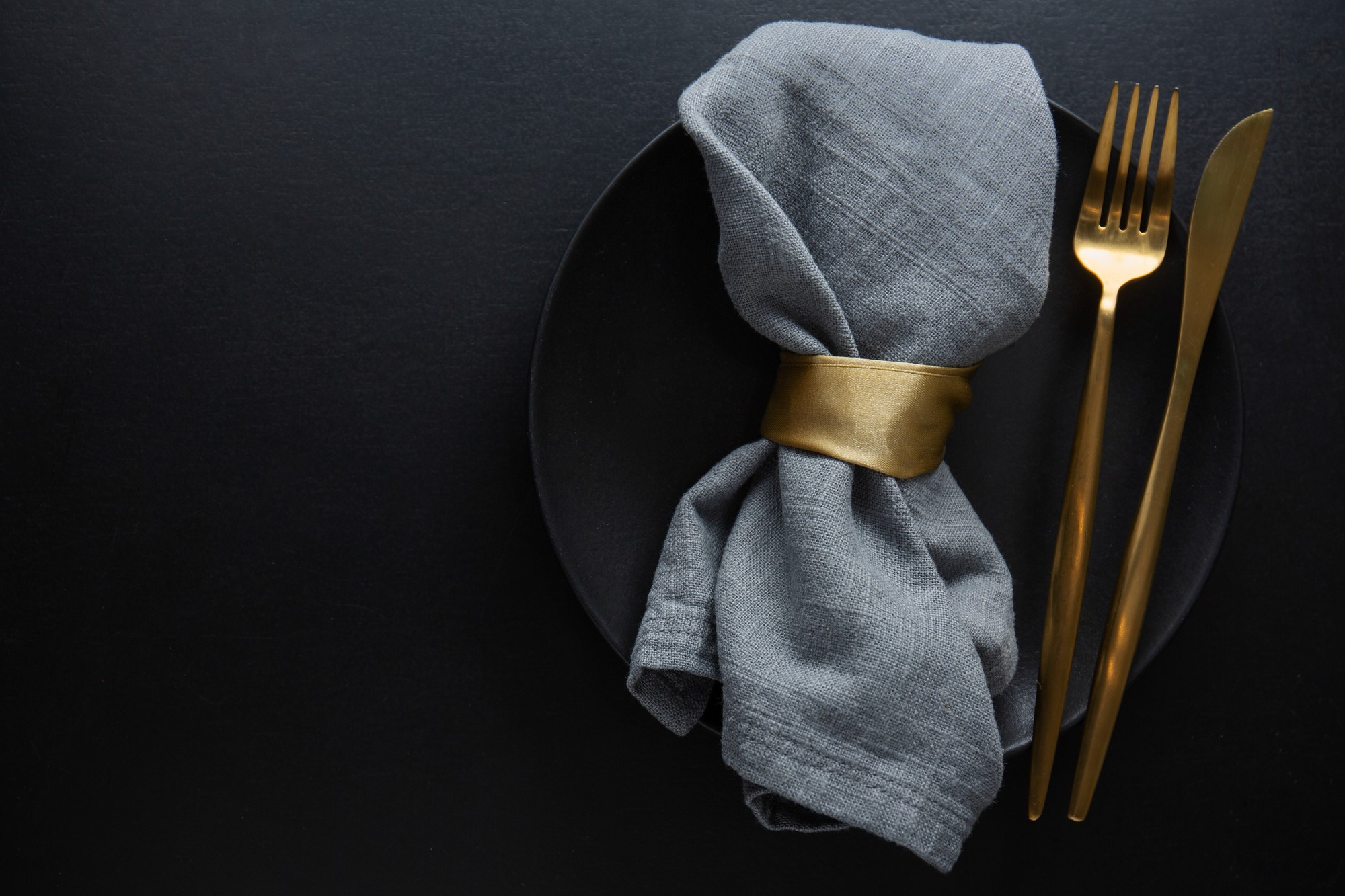 golden-cutlery-with-textile-plate-dark-background-top-view